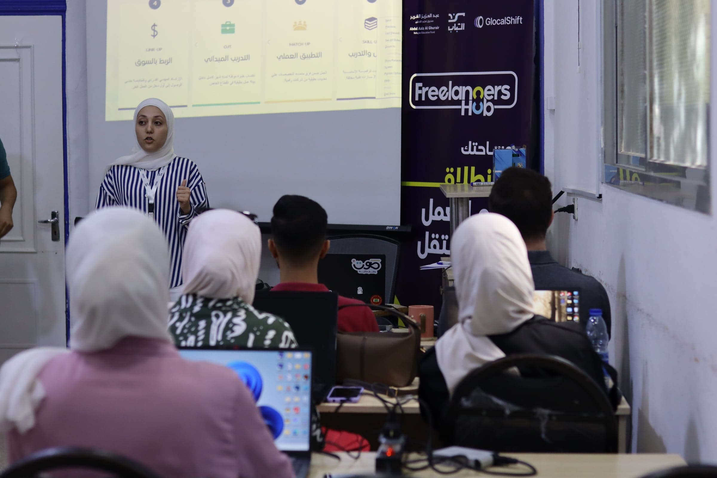 مدرّبة تقدّم جلسة تدريبية لمشاركين في Freelancers Hub يجلسون أمام حواسيبهم المحمولة